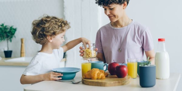 Happy family mother and son eating cereal with milk at home talking